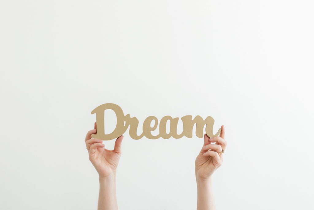 Branding photo against white background of hands holding a sign that says dream.